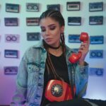 Fashionable woman in denim holding a vintage rotary phone, surrounded by cassette tapes.